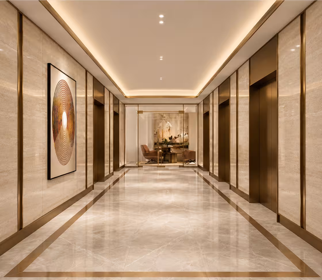 The residential lift lobby at Cappella Embassy — marble walls with brass inlay, warm cove lighting and a seating vignette at the end of the corridor